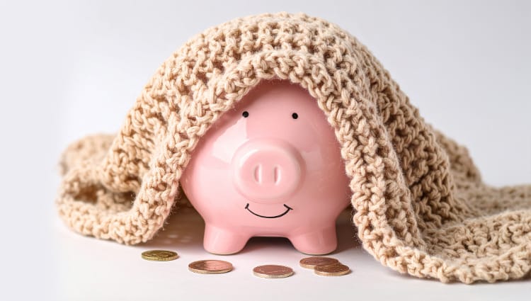 Porquinho de cofrinho rosa com cobertor de crochê, simbolizando uma reserva de emergência e segurança financeira