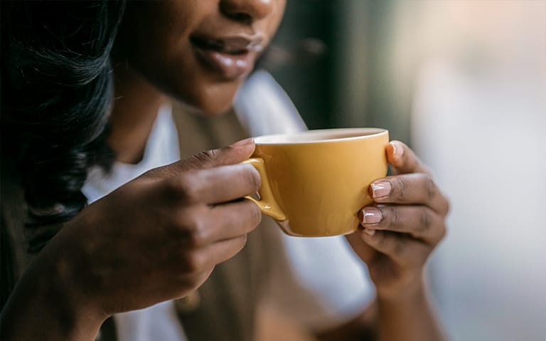 mulher tomando bebida quente em uma xícara amarela